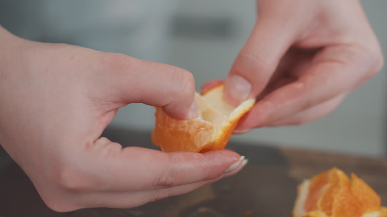 Primer plano de manos separando un segmento de membrana de naranja en la encimera, técnica cuidadosa con la punta de los dedos, manicura impecable, luz brillante de cocina, preparación de un tentempié, presentación limpia, estilo tutorial.