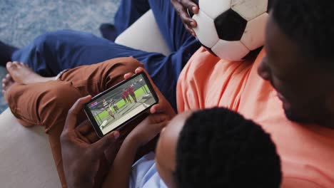 composite of father and son at home watching rugby match on smartphone