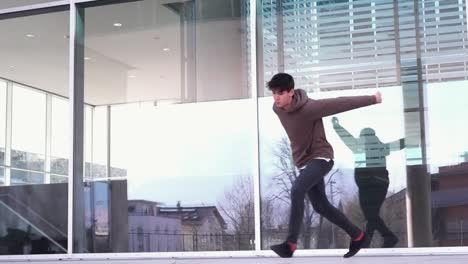 joven atleta de parkour haciendo un corcho frente a una pared de vidrio en cámara lenta