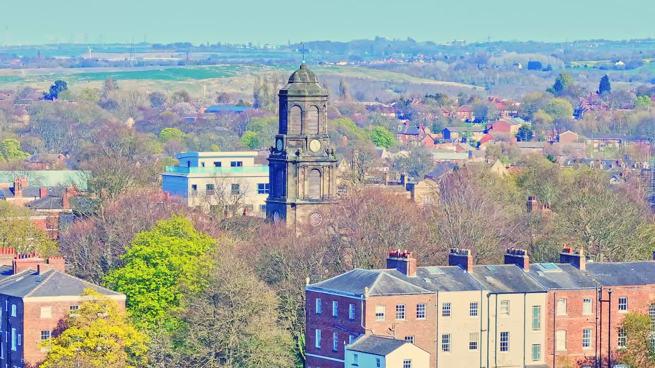Aerial view of a historic stone church in Wakefield, Yorkshire, England, surrounded by blooming spring trees and lush countryside under clear sunlight.