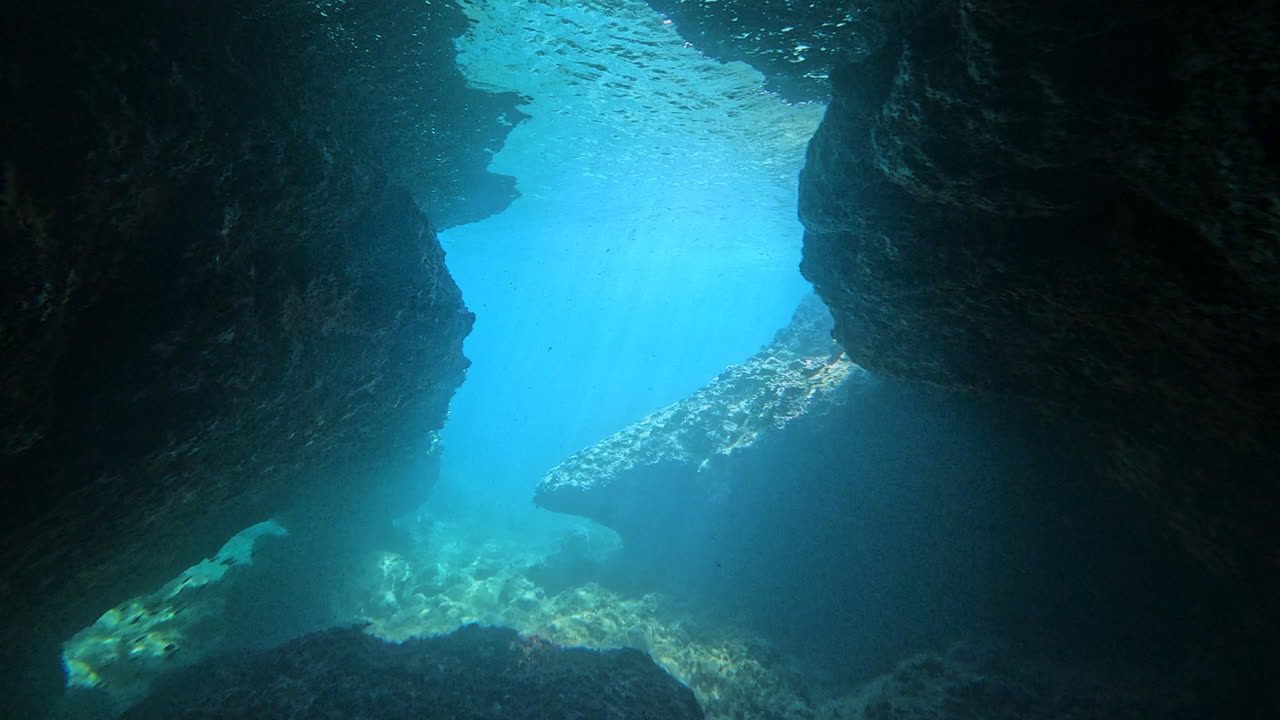 Rocky underwater cave passage with light shining into the open blue sea. Great for adventure, exploration, diving, and marine environment themes