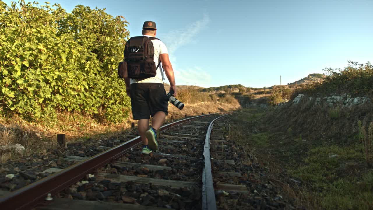 fotógrafo solitario mochilero en interminable vía férrea, vista trasera