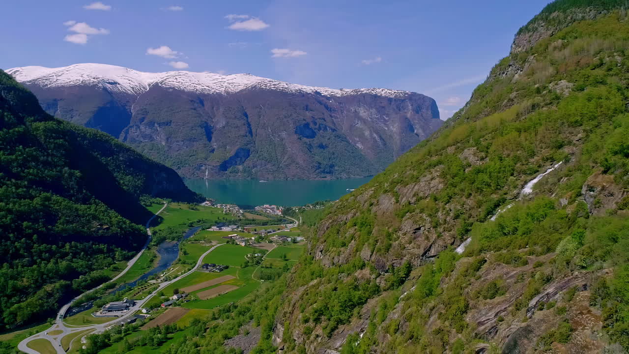 cascada escondida entre las altas montañas verdes con en el fondo el tranquilo aurlandsfjord