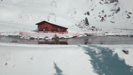 Zurückweichende-Drohnenaufnahme-Einer-Hütte-Neben-Einem-Künstlichen-See-Und-Neigung,-Um-Die-Kiefern-An-Seinem-Hang-Zu-Zeigen,-In-Engelberg-Brunni,-Bahnen-In-Der-Schweiz