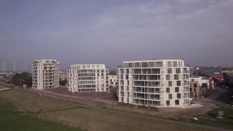 sideways aerial pan showing rising exterior facades of newly build luxury apartment towers pracht along riverside of river ijssel seen from above