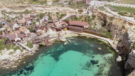 Mediterranean-shore-of-Anchor-Bay-on-Popeye-Village-in-Malta---Aerial-orbit-shot