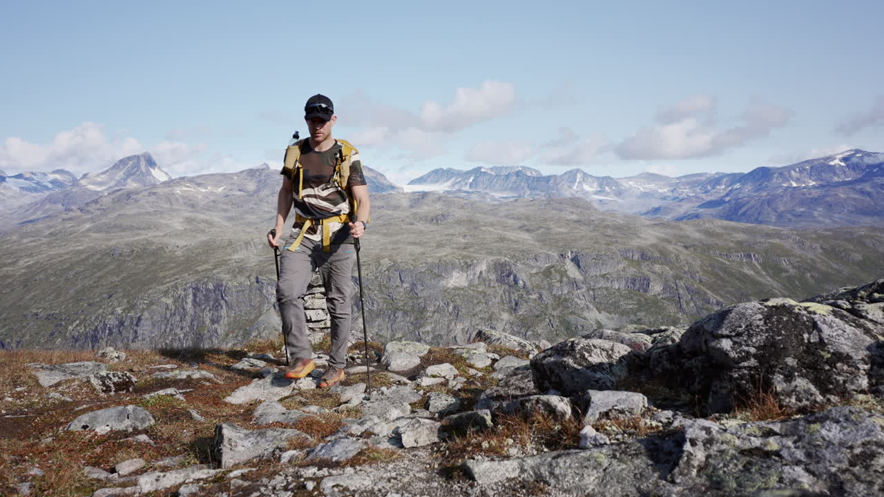 vista amplia y lejana de un hombre caminando más allá de un cairn con un fondo montañoso durante el día