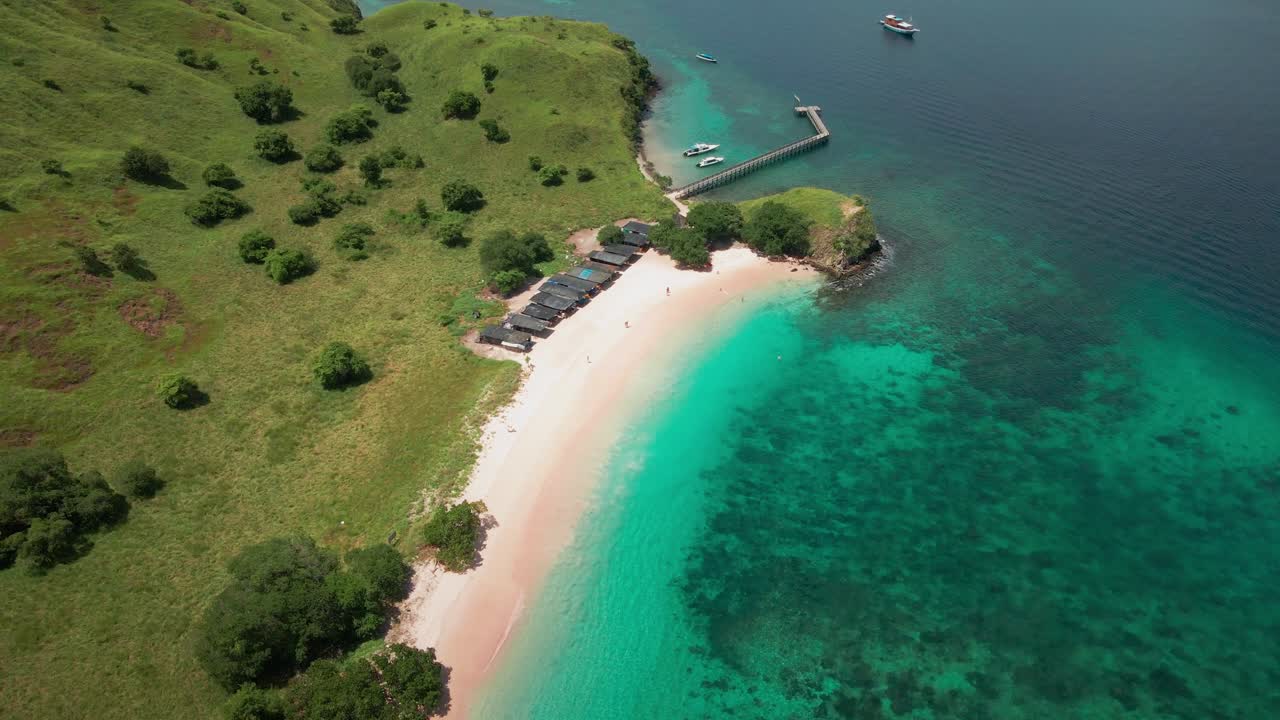 Komodo Milli Parkı, Flores'teki güzel Pembe Plaj'ın nefes kesen havadan görünümü—kristal berraklığında turkuaz sular, yemyeşil tepeler ve açıkta demirlemiş bir tekneye uzanan ahşap bir iskele.