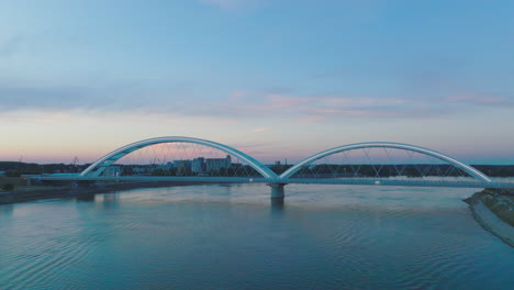 modern arch bridge over river at sunset