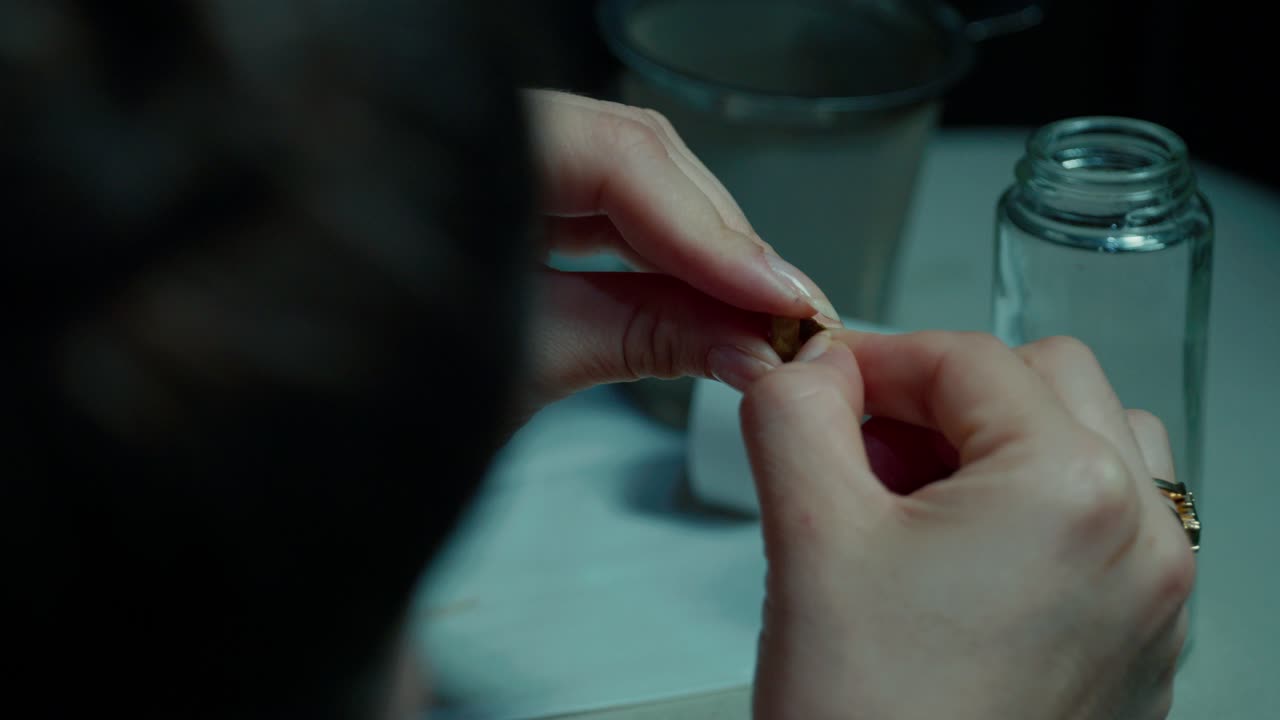A close-up shot of a young girl's hands examining cardamom pods under soft, warm lighting. The detailed view captures the texture and color of the spices, evoking an aromatic atmosphere
