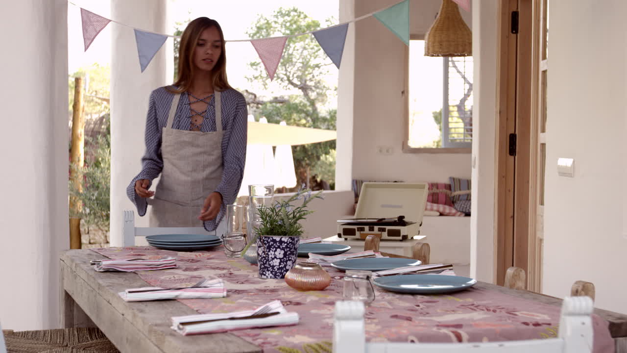 una mujer joven preparando la mesa en una terraza para una cena, filmada en r3d
