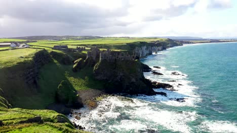 flying over ireland’s wild coastline with clear view of crashing waves and rock faces, dunluce castle establishing aerial