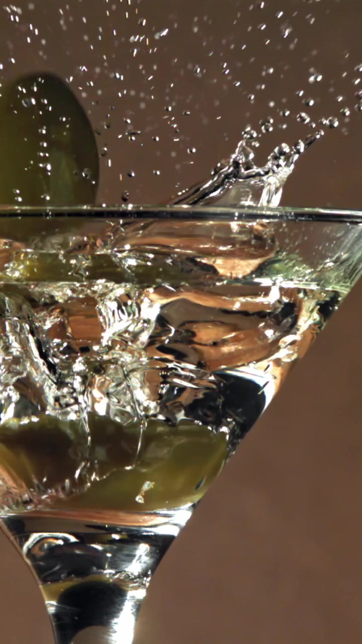 Oliva verde che si tuffa in un cocktail Martini trasparente al rallentatore