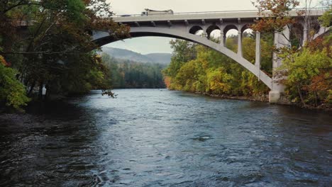 Aerial-shot-of-a-bridge-over-Housatonic-river-passing-with-the-view-of-hilly-terrain-in-the-background-in-Litchfield-County,-Connecticut,United-States