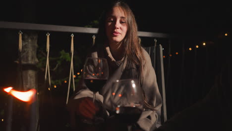 a woman relaxing on a balcony at night with a glass of wine and candles