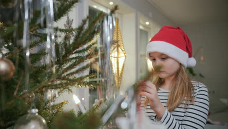 young blonde girl in santa hat decorates christmas tree, close up