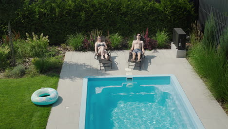 Young-couple-relaxing-by-the-pool,-lying-on-sun-loungers-and-sunbathing