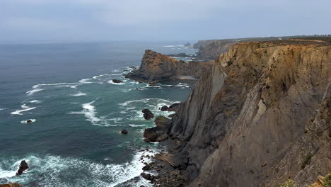 tilt down shot of gigantic steep cliff coastline in sagres with crashing waves in portugal - aerial top down - most south western point in europe