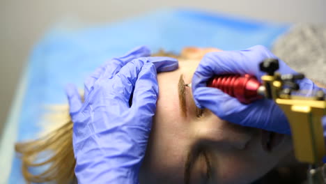 tattooist making permanent make-up. close up of specialist doing eyebrow tattooing for female