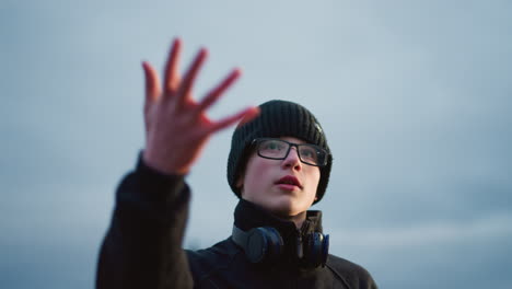 a close-up of a young boy in a black outfit and glasses with head set on his neck, lifting a soccer ball in the air, with a blurred view of lights in the background