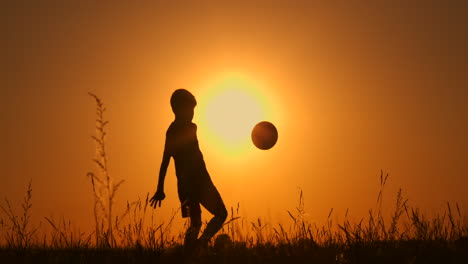 A-young-young-boy-football-player-trains-playing-with-a-ball-stuffing-on-his-leg-at-sunset-in-slow-motion-during-the-Golden-hour-in-the-field-until-sunset.-Training-from-dusk-to-dawn.-Concept-path-to-success