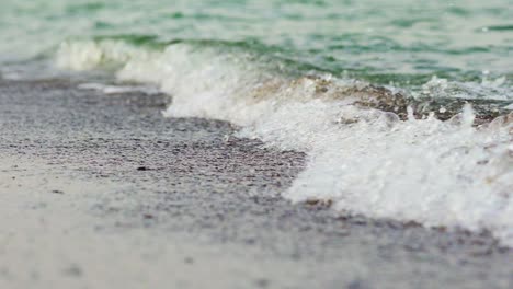 a turquoise sea waves cover the coast and take small grains of sand with it. close-up. blurred background.