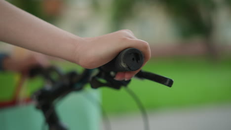 close-up of person s hand gripping bicycle handlebar while strolling along park pathway with mint-colored bag visible, set against blurred greenery background