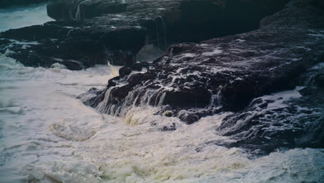 White-ocean-washing-rocks-on-storm-day.-Closeup-foaming-waves-hitting-coastline