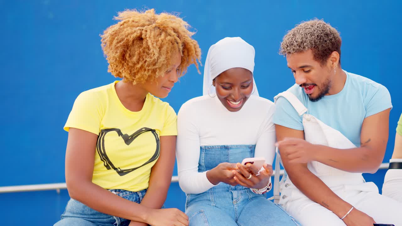 Multi-ethnic friends using phone and smiling sitting on a wall