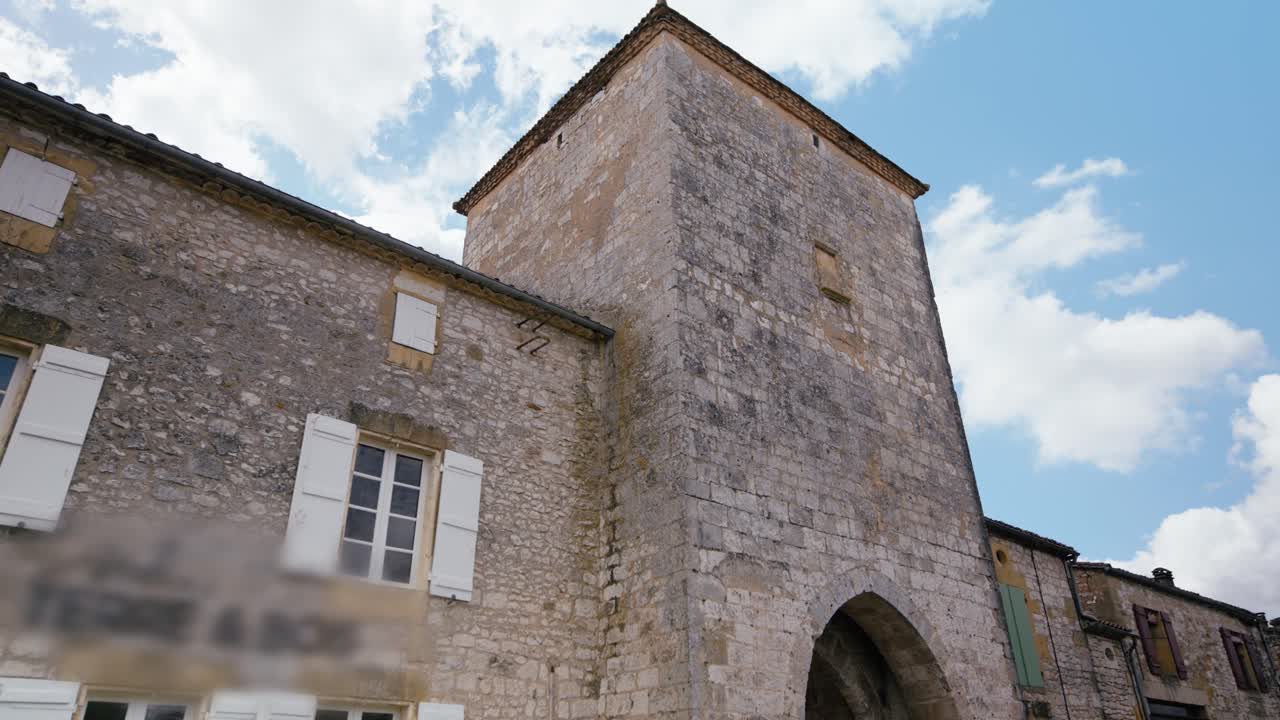 Torre in pietra e arco di una struttura medievale a Monpazier, Dordogna. Questa scena mostra la muratura storica sotto un cielo nuvoloso. Carrellata al rallentatore.