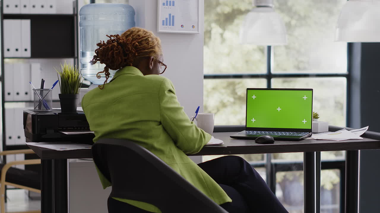 Woman working on laptop with green screen in office
