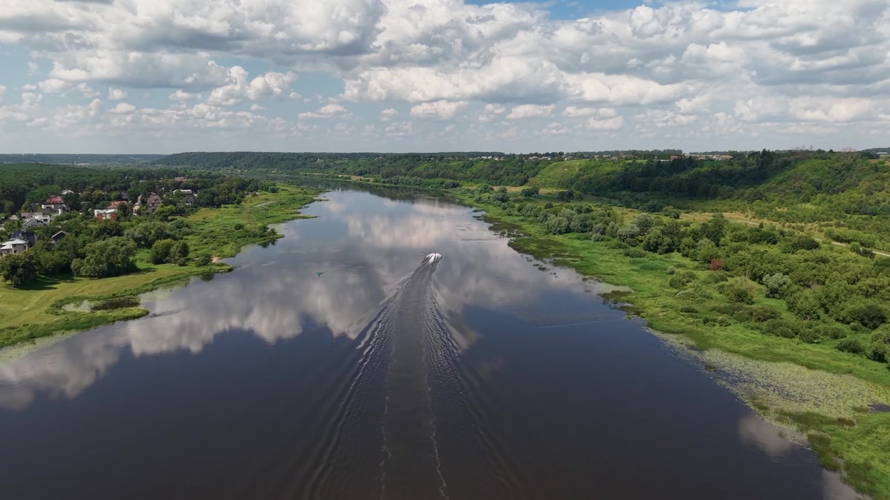 Fantastisk dronevideo viser en ensom båd, der glider ned ad en rolig flod, frodigt grønne bredder og reflekterede skyer. Bredt panoramaudsigt, levende dagslys, fredfyldt stemning, skarpe luftoptagelser