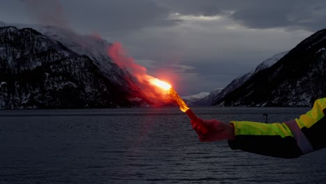 Miembro-De-La-Tripulación-Del-Barco-Sosteniendo-Una-Bengala-De-Emergencia,-Fondo-Del-Fiordo-Invernal-Por-La-Noche