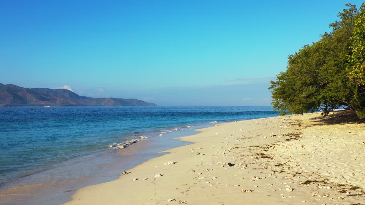 Tranquil exotic beach of tropical island with white sand washed by waves of blue sea under clear bright sky, Indonesia