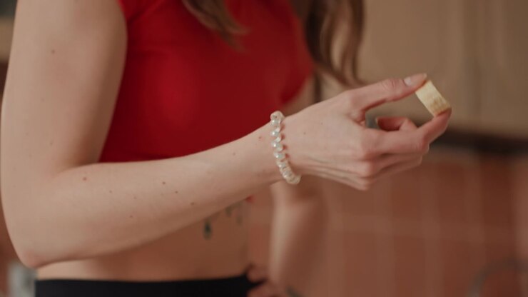 Donna in cucina di casa che assaggia un piccolo spuntino, momento contemplativo di controllo delle porzioni con contenitore trasparente sul bancone, top rosso casual, ruolo di studentessa di nutrizione, decisione consapevole, luce interna calda, primo piano.