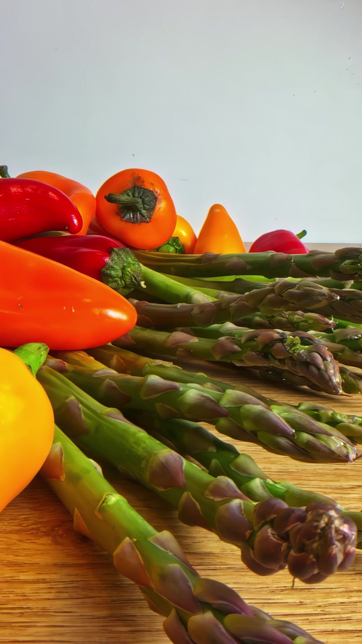 Un gatto grigio attraversa l'inquadratura dietro file di asparagi freschi e vivaci mini peperoni, catturando una scena di cucina inaspettata e affascinante.