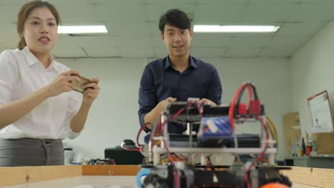 two electronics engineer programming and control robots to playing soccer with mobile phone in the workshop. people with technology or innovation concept.