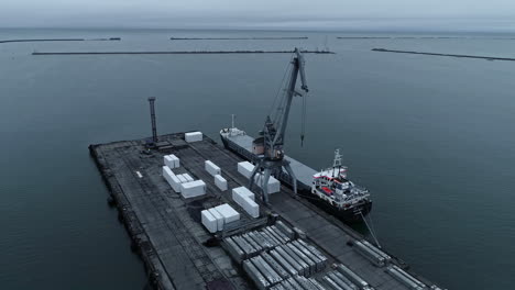 aerial drone rotating shot over shipping containers being been loaded onto a container ship in a harbour during evening time