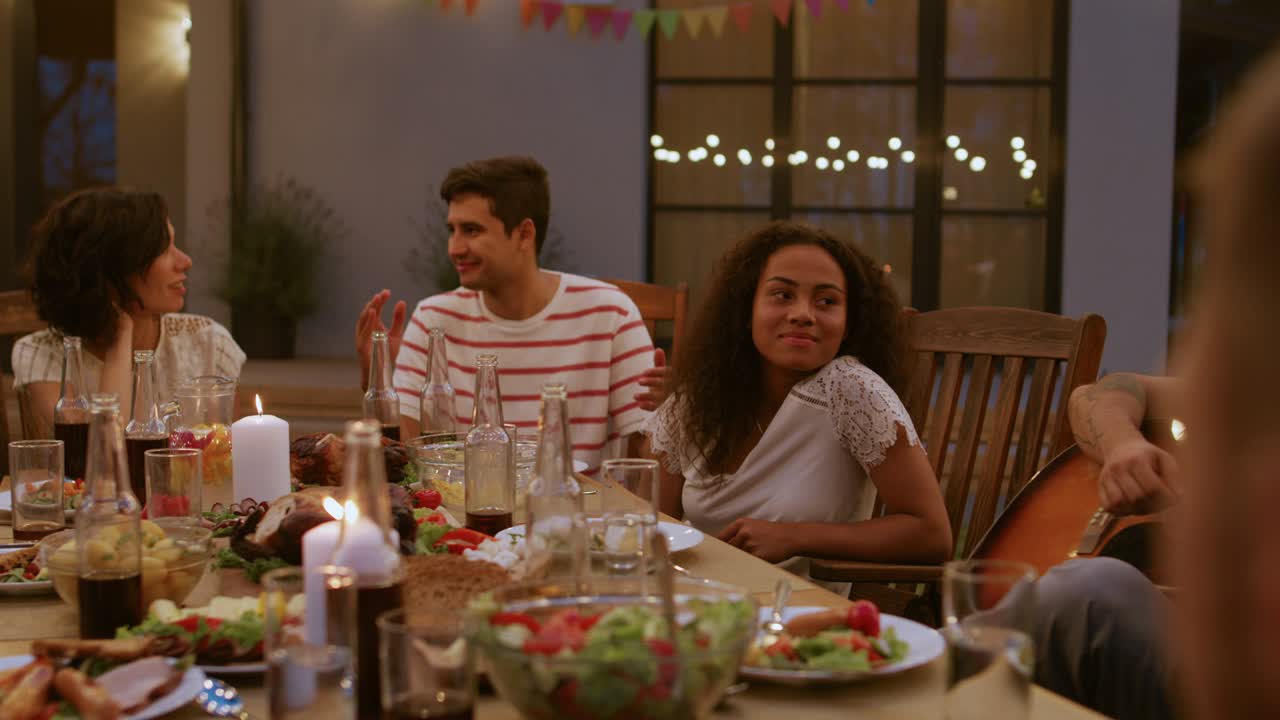 gran celebración de fiesta de jardín familiar, reunidos en la mesa parientes y amigos, jóvenes y ancianos están comiendo, bebiendo, pasando platos, bromeando y divirtiéndose. luces decorativas encendidas esta noche.