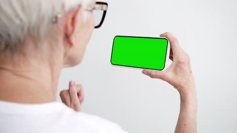 old person touch and swipe screen smartphone with green chroma key close-up. older 50s female hold in hand cell phone clicking mock-up. concept watch and show gallery social media, read news, app 4k