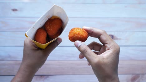 hand holding a paper container of spicy fried chicken nuggets