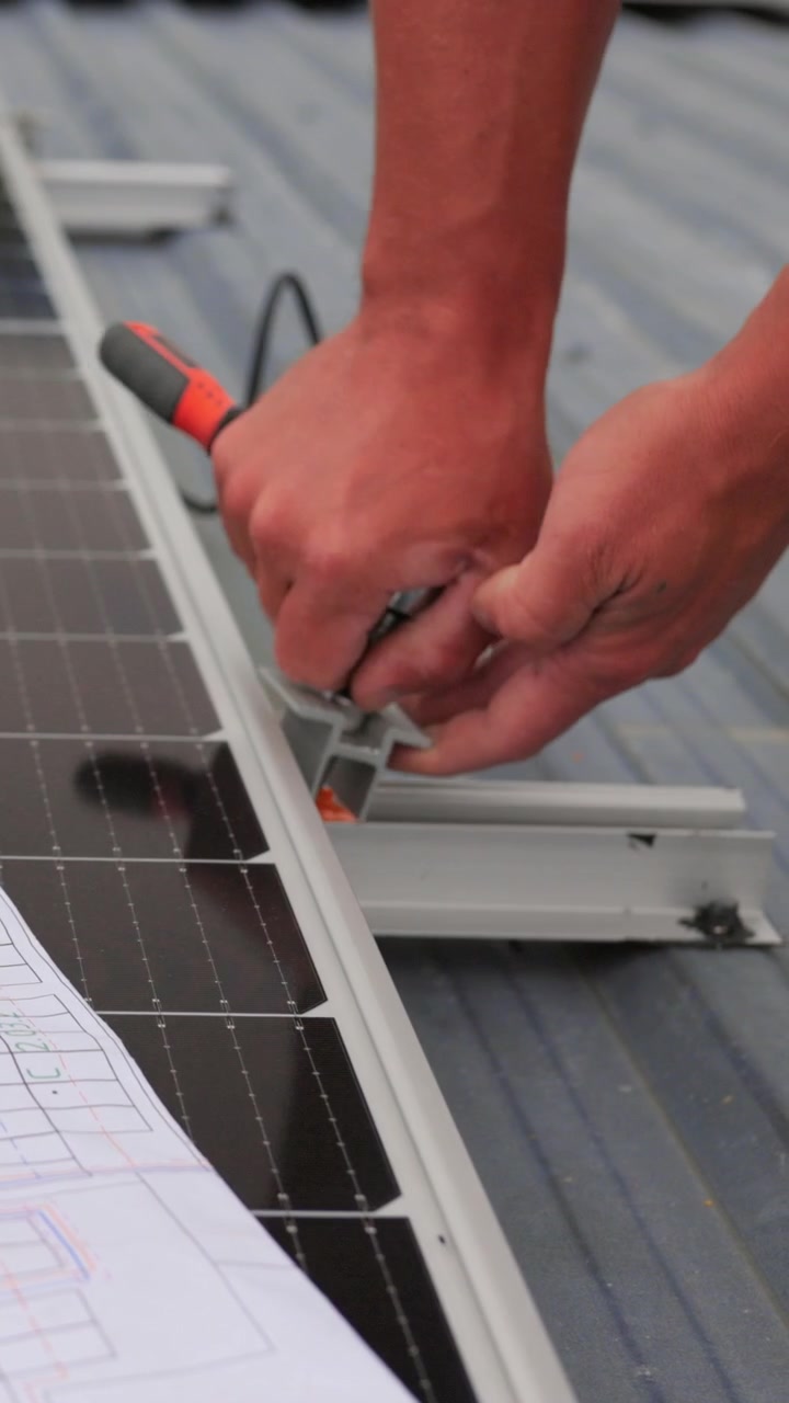 A worker is installing solar panels on a rooftop using a screwdriver to secure the components this