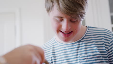 Young-Downs-Syndrome-Man-Decorating-Homemade-Cupcakes-With-Icing-In-Kitchen-At-Home