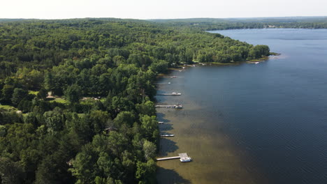 Vista-Aérea-Panorámica-De-Alto-ángulo-De-Muelles-Privados-Que-Llegan-Al-Agua-Azul-Profunda-Desde-Colinas-Boscosas-En-Maple-Lake-Ontario