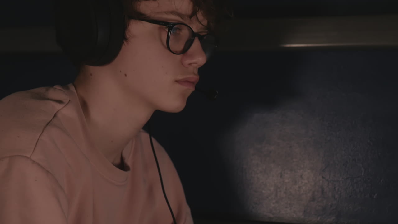 incline hacia arriba desde el controlador de videojuegos hasta la cara de un adolescente con audífonos y anteojos