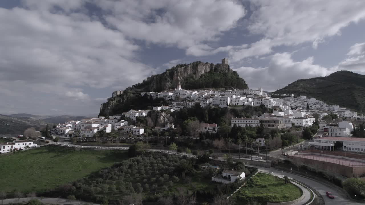 Low-altitude frontal 4K drone shot of Zahara de la Sierra, Spain, filmed with a DJI at 30fps. A cinematic view of the charming village with its historic castle in the background.