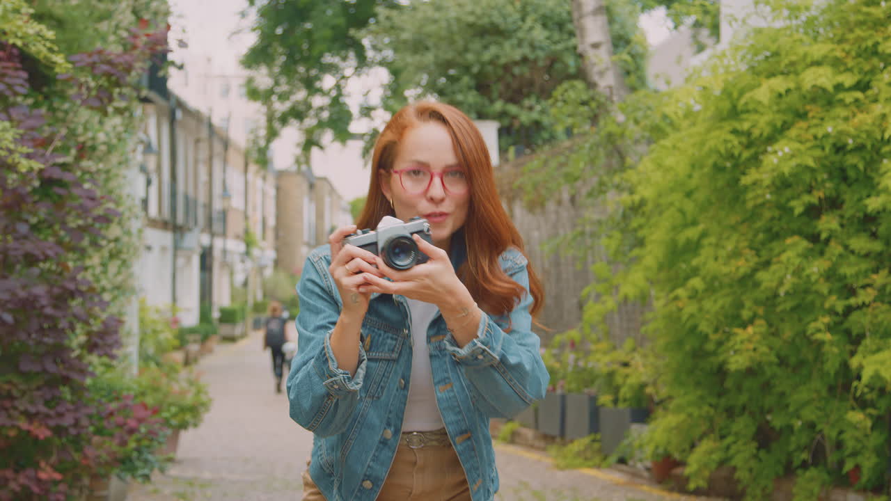 Mujer joven en la ciudad tomando fotos con una cámara digital para publicar en las redes sociales