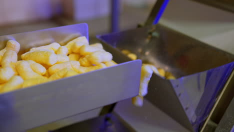 Manufacturing sweet snacks at modern factory. Delicious crispy maize sticks falling on conveyor belt. Close up.