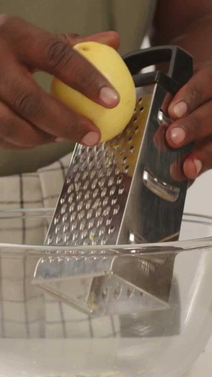 Video verticale: Uomo in maglietta verde che grattugia un limone per la scorza, posizionando una grattugia a scatola sopra una ciotola.