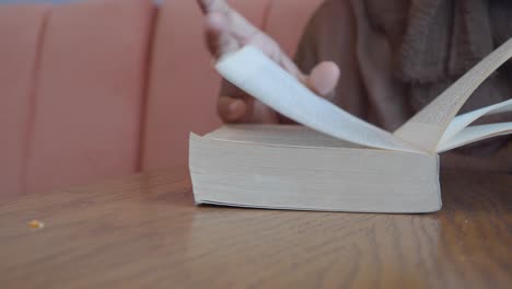 person's hand flipping pages of a book on a table
